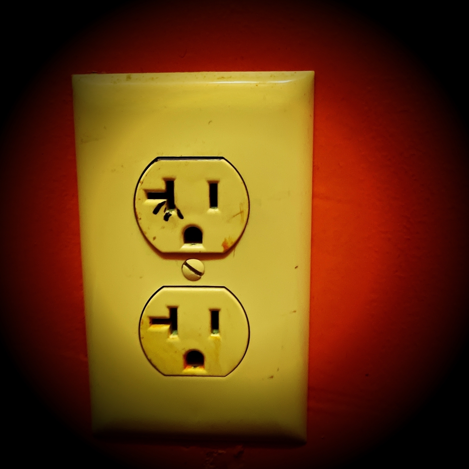 A discolored and cracked electrical outlet is set against a vivid red background.